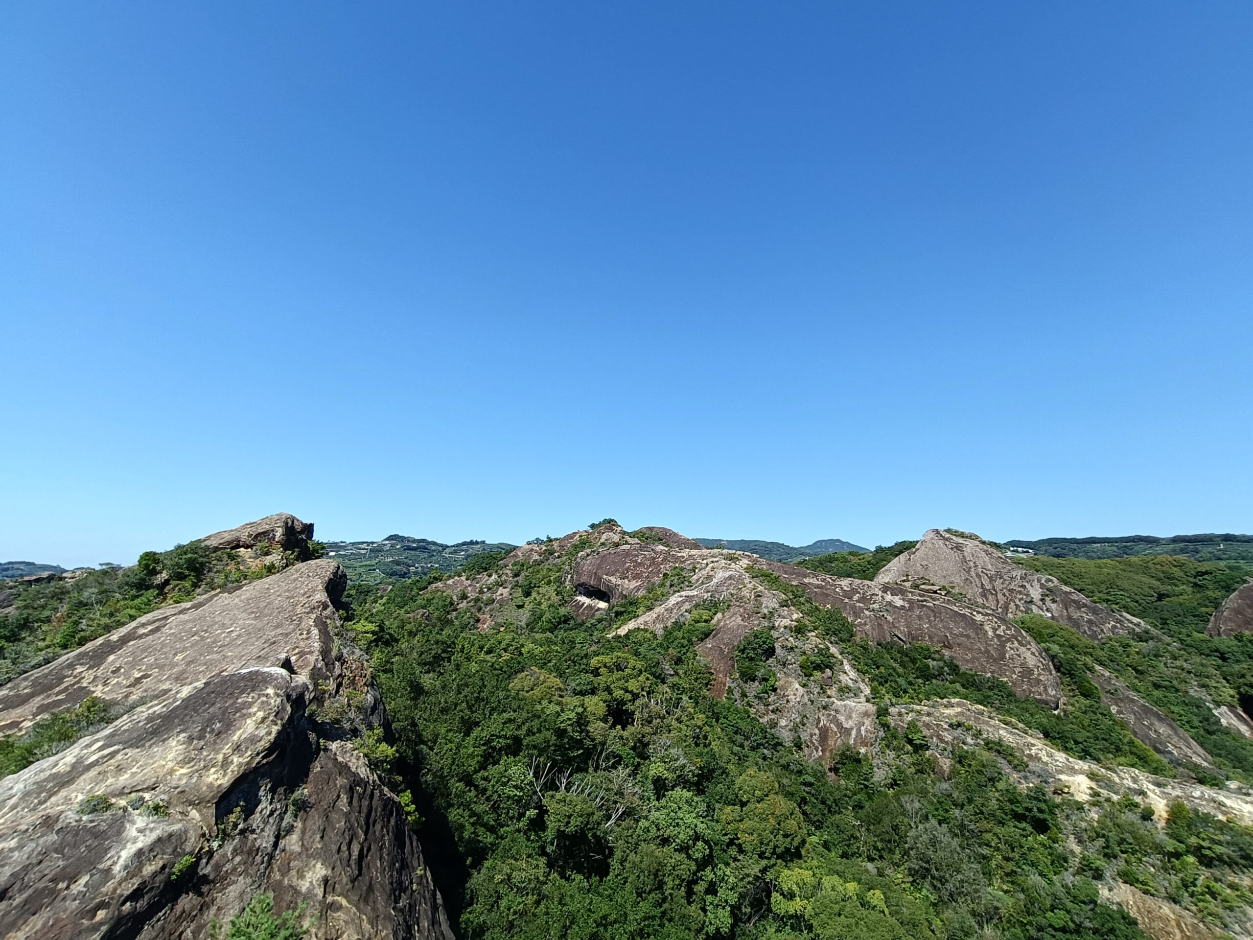 青空の下に岩肌と緑の木々が連なる丘陵